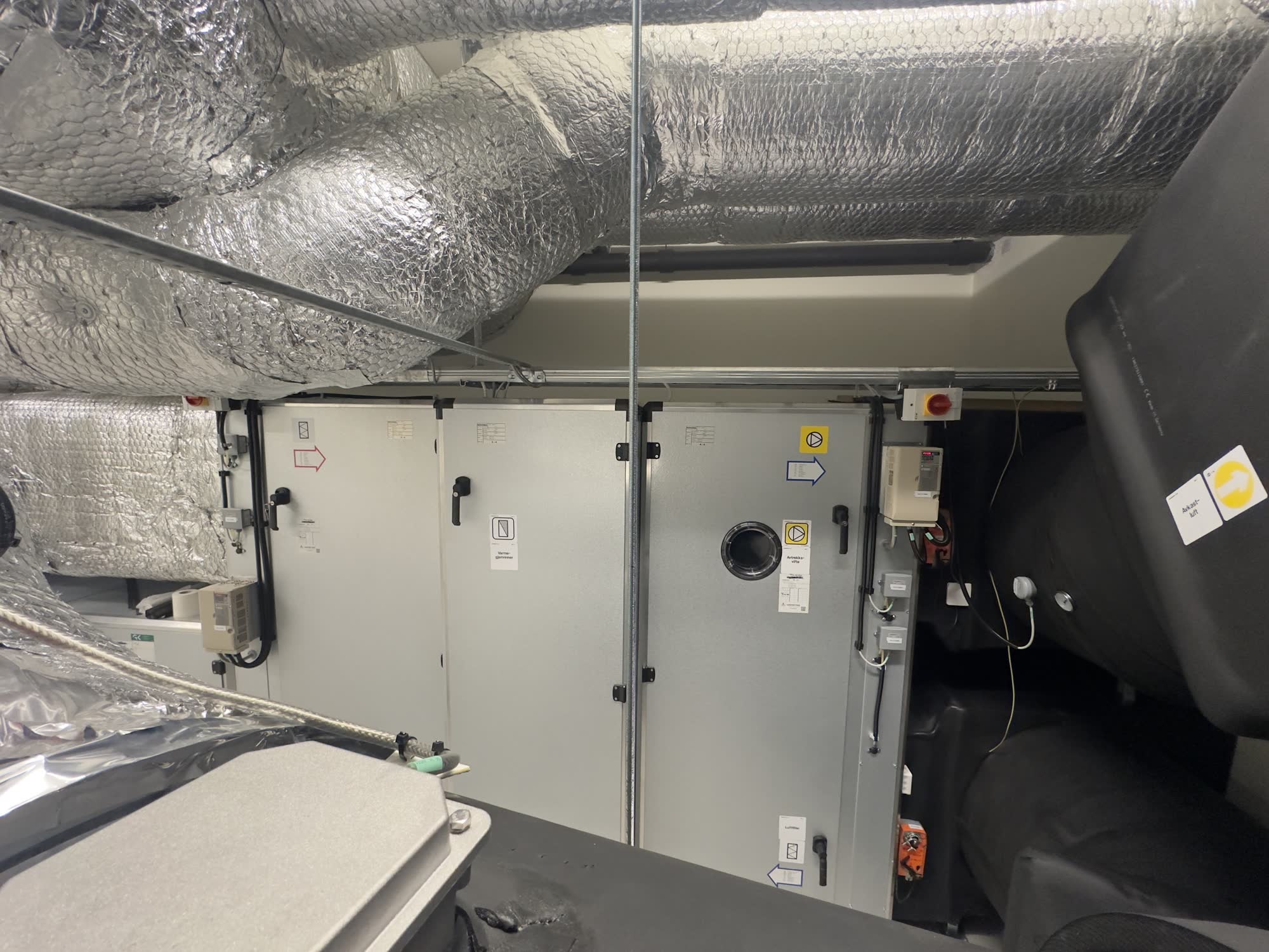 Insulated silver ductwork running along a ceiling with pipes and cable trays