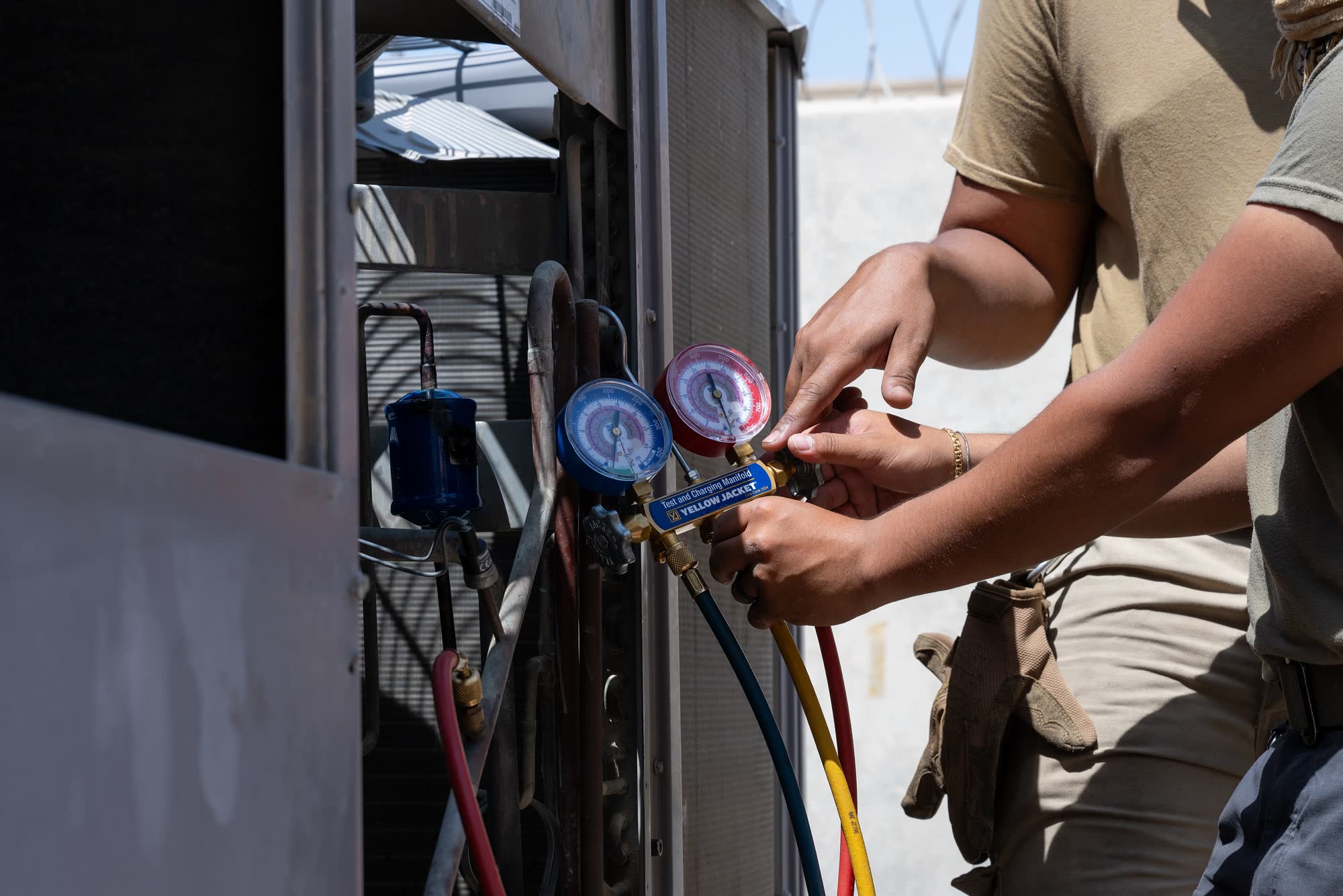 Technician connecting refrigerant manifold gauges to an outdoor condenser
