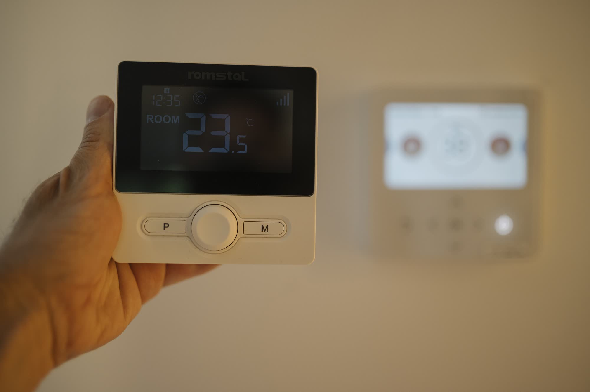 Hand holding a wall thermostat that reads 23.5 degrees